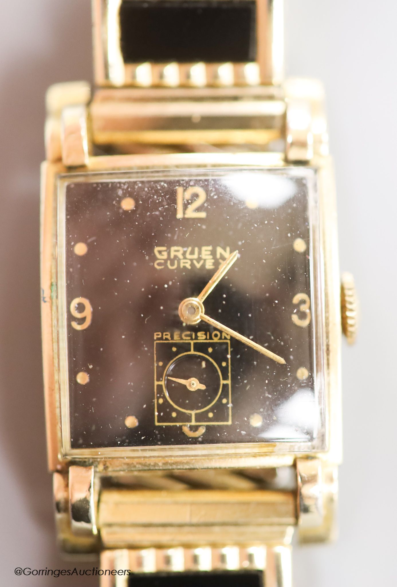 A gentleman's 1930's 10k gold filled, stainless steel Gruen Curvex Precision manual wind rectangular black dial wrist watch, on a gold plated and ceramic bracelet.